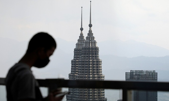 A man uses his phone as the Petronas Twin Towers are seen in the background in Kuala Lumpur, Malaysia April 12, 2021. Photo by Reuters